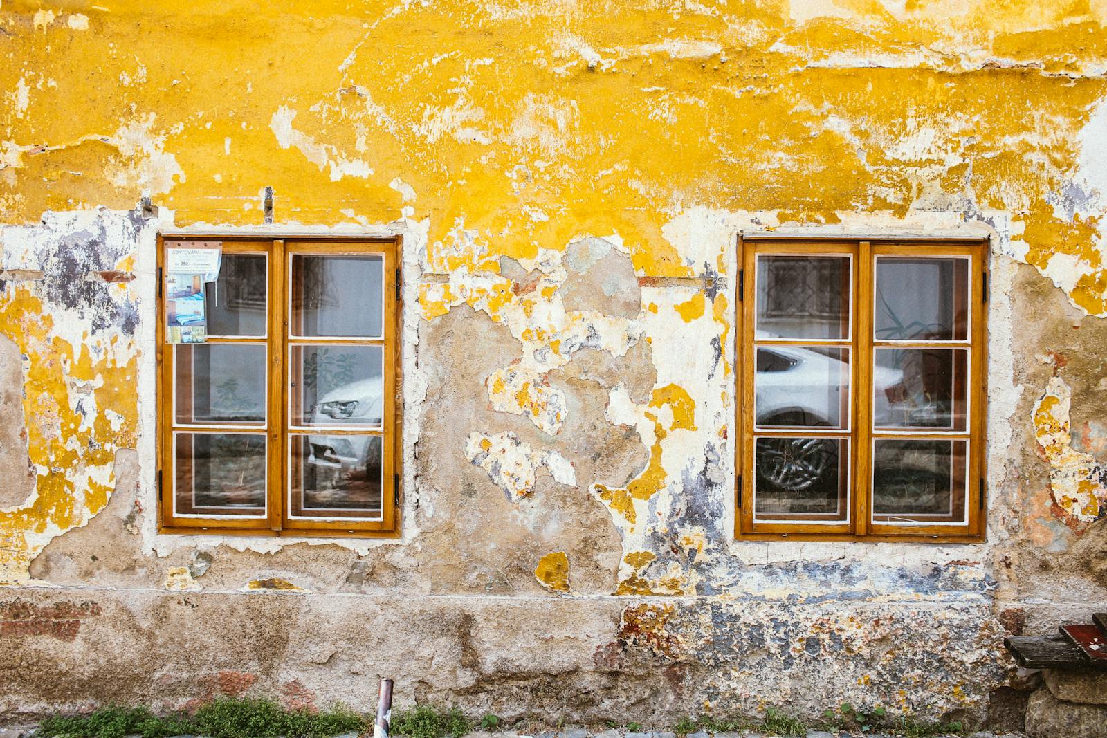 Old textured wall with rustic windows showcasing peeling paint and reflections.