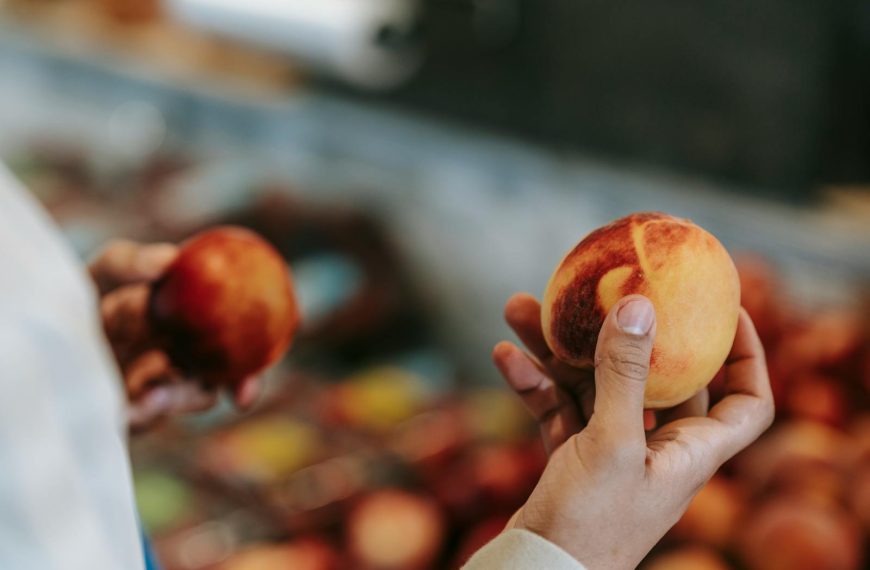 Man selecting fresh peaches with blurred market background.