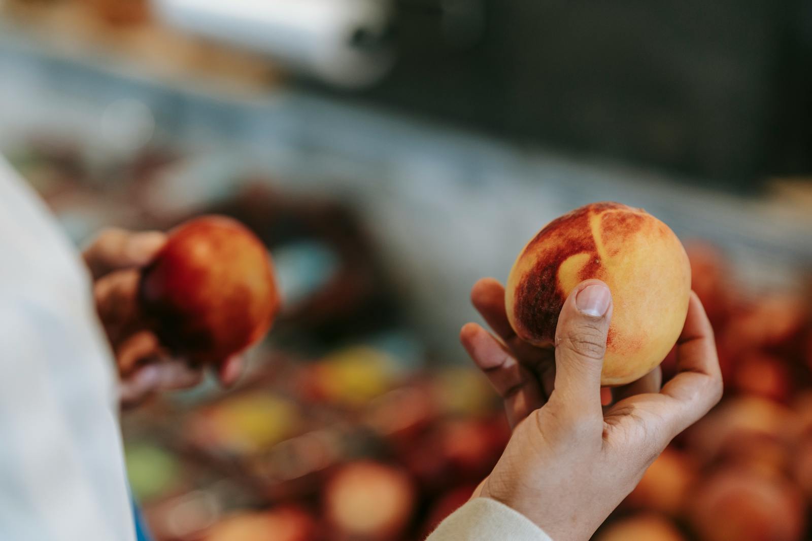 Man selecting fresh peaches with blurred market background.