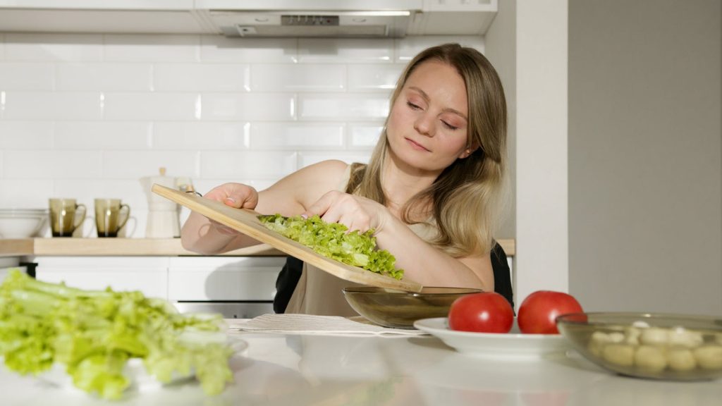 A woman preparing a fresh salad with lettuce and tomatoes in a modern kitchen.
