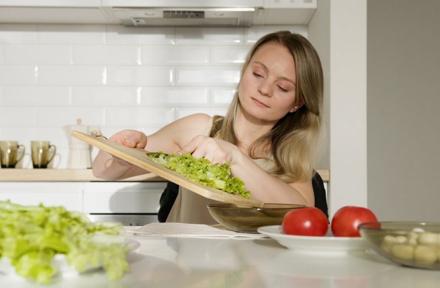 A woman preparing a fresh salad with lettuce and tomatoes in a modern kitchen.