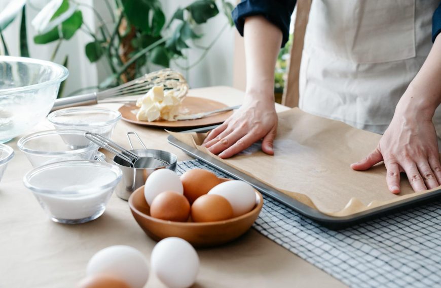 Hands preparing baking tray with ingredients ready for baking, including eggs and flour.
