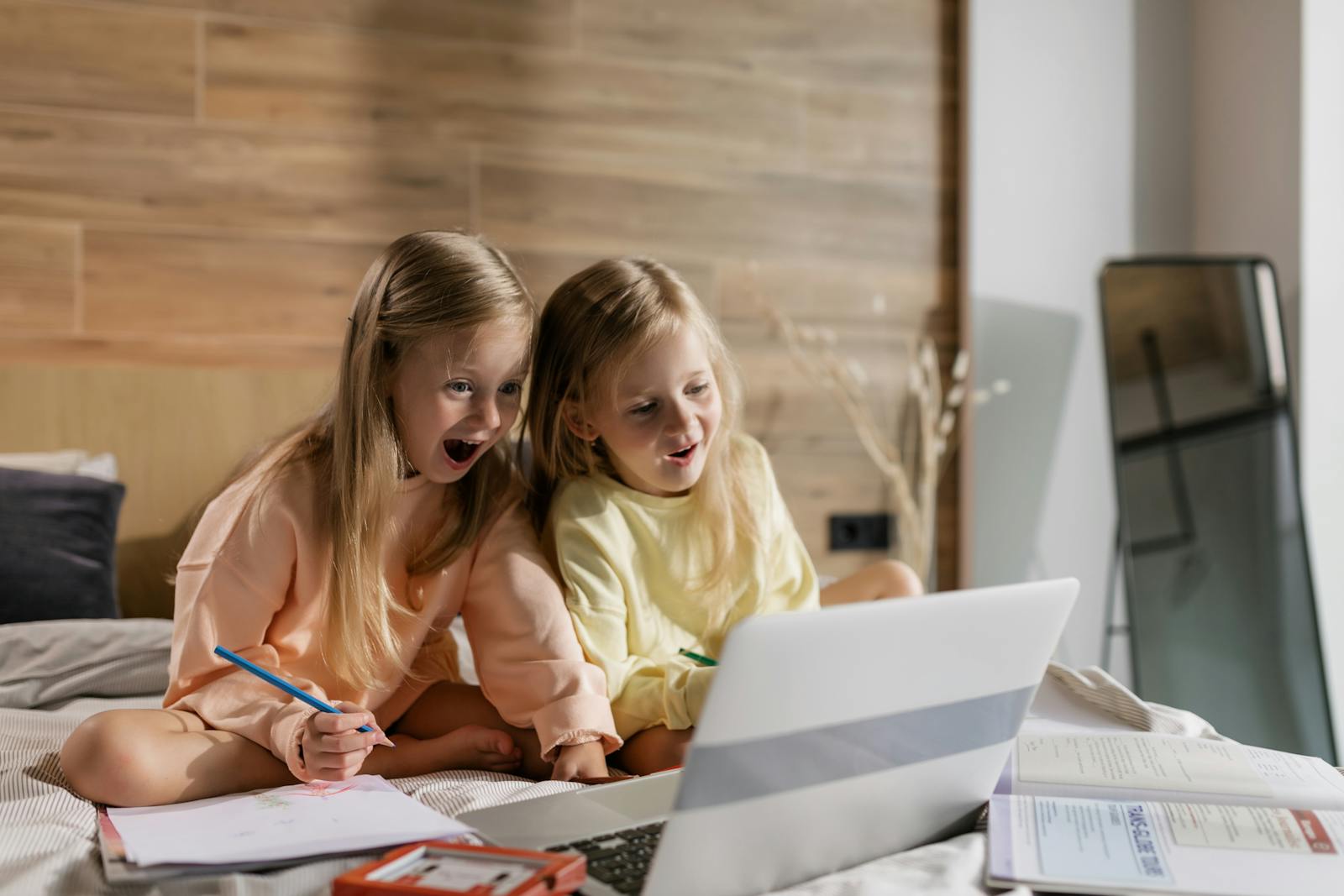 Happy twin girls indoors, excitedly learning on a laptop, showcasing the fun in online education.