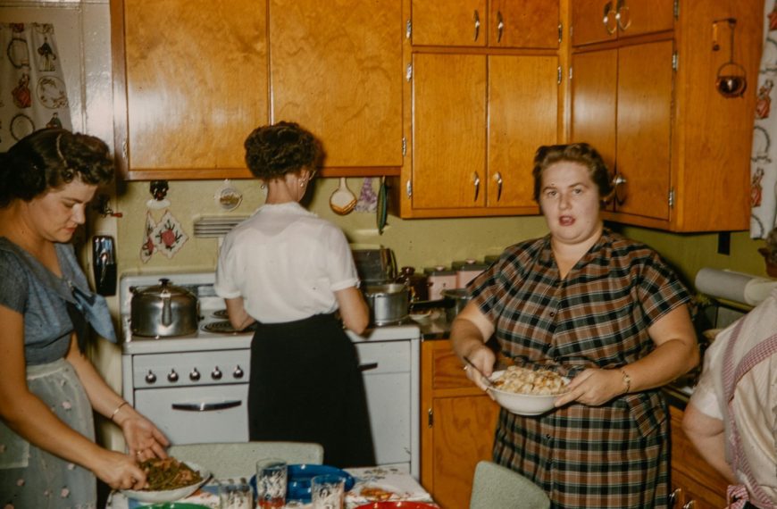 a group of women standing around a kitchen preparing food