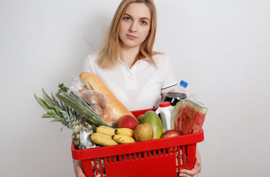 woman in white long sleeve shirt holding red plastic basket with fruits