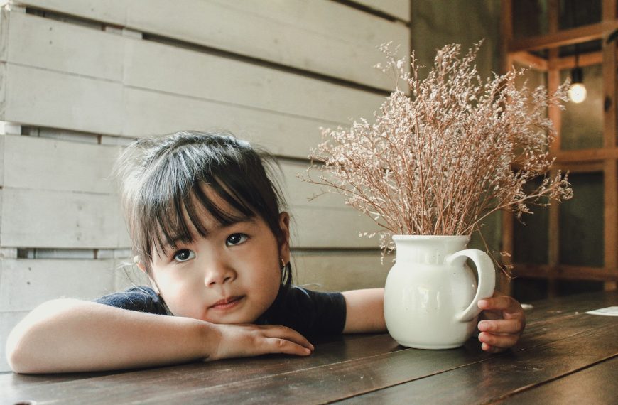 girl in black sleeveless shirt sitting beside white ceramic mug