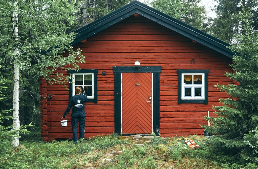 man in black jacket standing beside brown wooden house during daytime