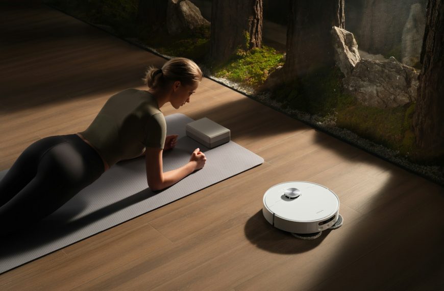 Woman planks on mat near robot vacuum cleaner.