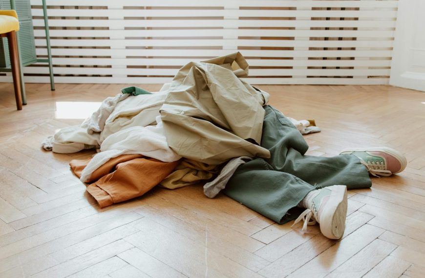 Pile of casual clothes on a wooden floor in a minimalistic room.