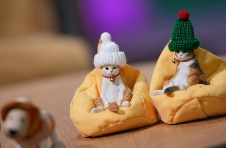 Two cat figurines wearing hats sit comfortably in bean bags, creating a cozy scene.