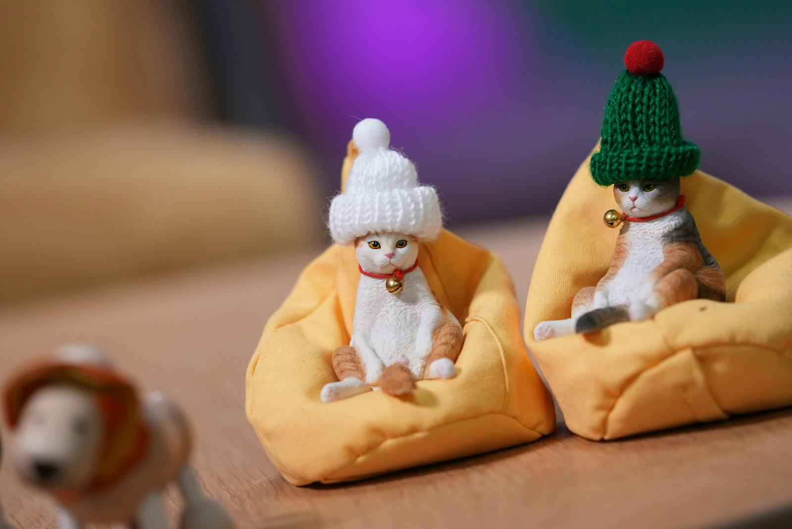Two cat figurines wearing hats sit comfortably in bean bags, creating a cozy scene.