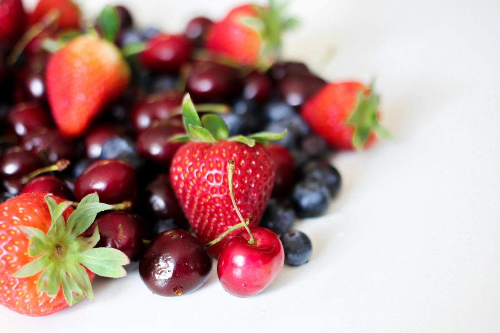 Vibrant assortment of fresh strawberries, cherries, and blueberries on a white background, showcasing natural freshness and juiciness.