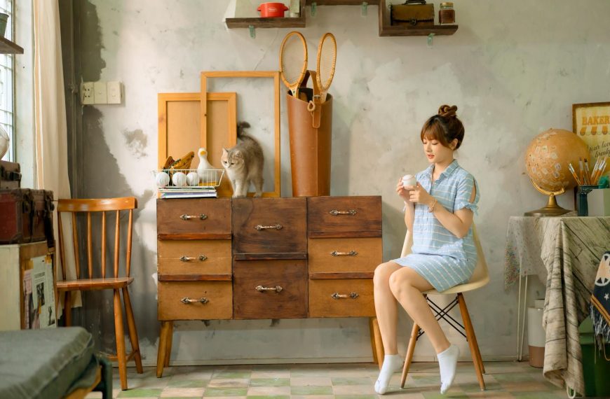 A woman sits in a vintage room with a cat, showcasing cozy interior decor.