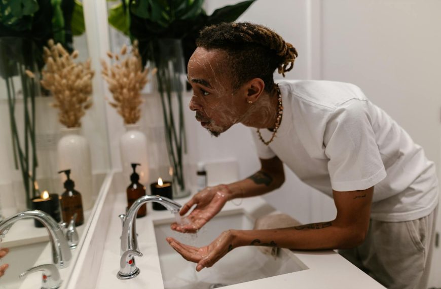 Man washing face in bathroom sink, showcasing a morning skincare routine for hygiene.