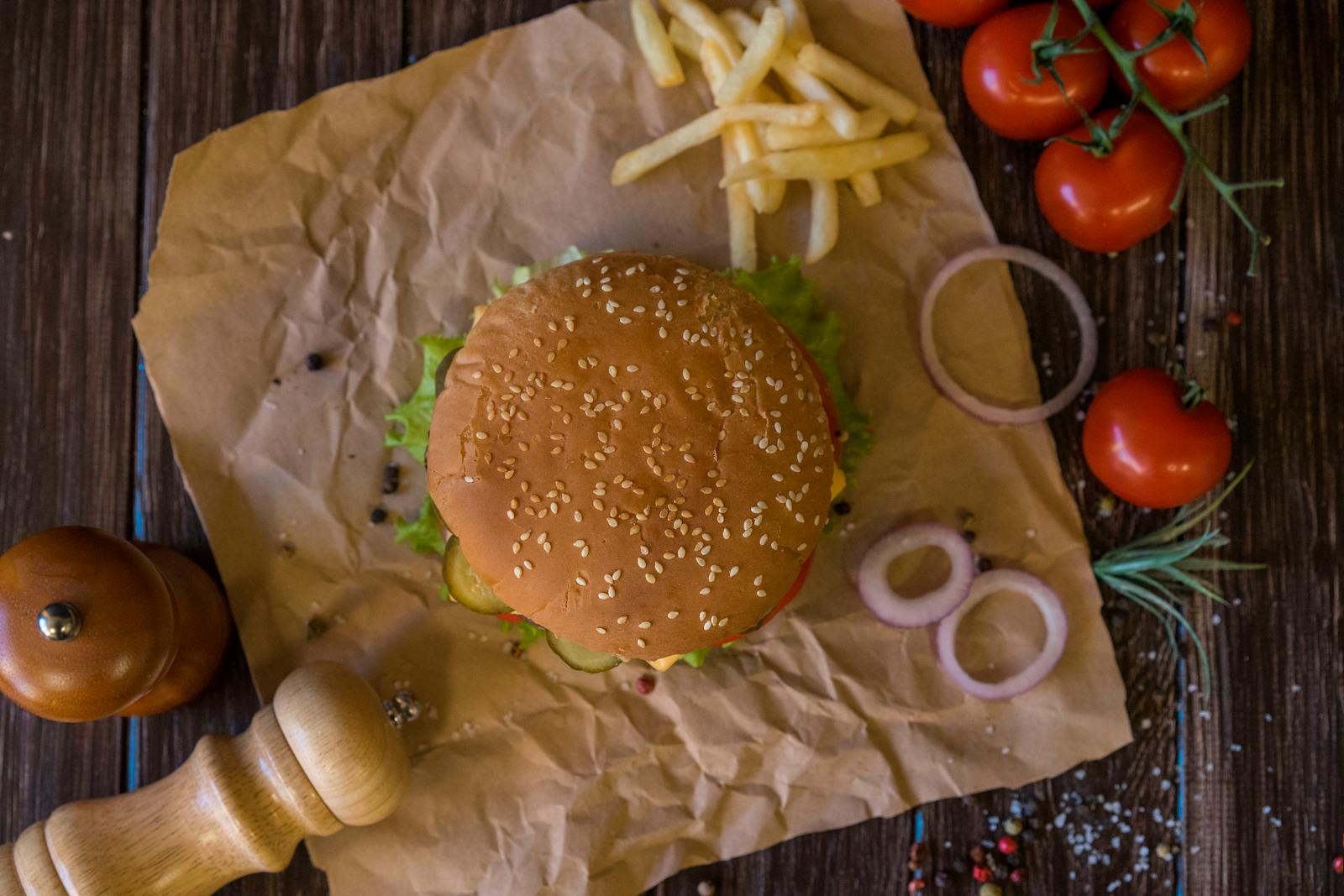 Top view of a tasty hamburger with fresh tomatoes and fries on a wooden table.