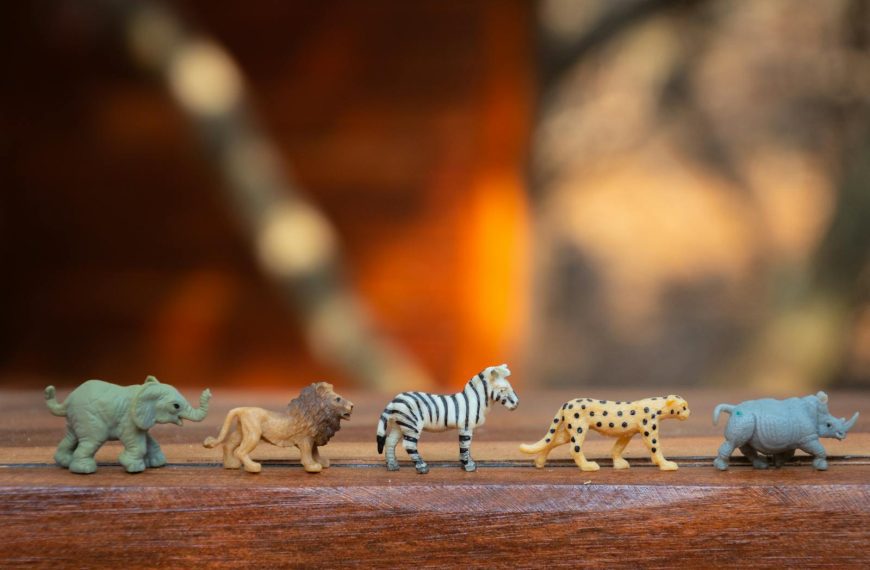 Miniature toy animals in a row on wood, displaying various wild species.