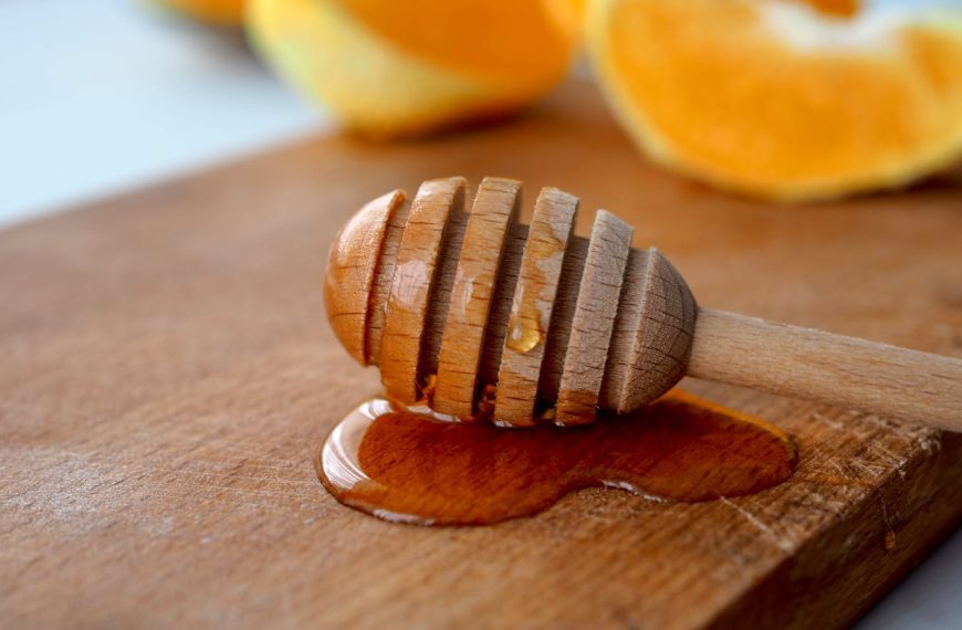 Close-up of a wooden honey dipper with honey on a rustic board and fresh citrus slices.