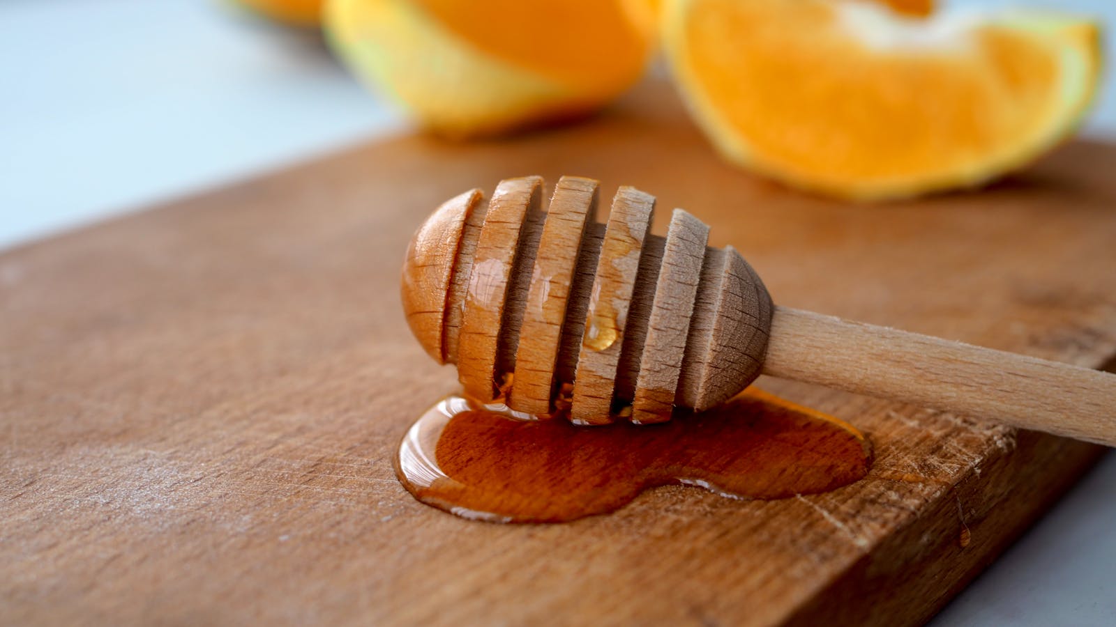 Close-up of a wooden honey dipper with honey on a rustic board and fresh citrus slices.