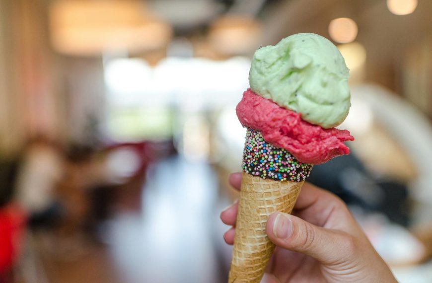 Hand holding a vibrant ice cream cone with sprinkles indoors, perfect summer treat.