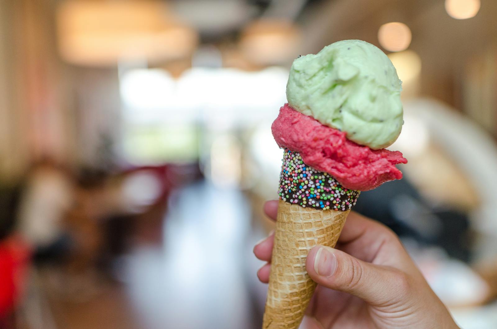 Hand holding a vibrant ice cream cone with sprinkles indoors, perfect summer treat.
