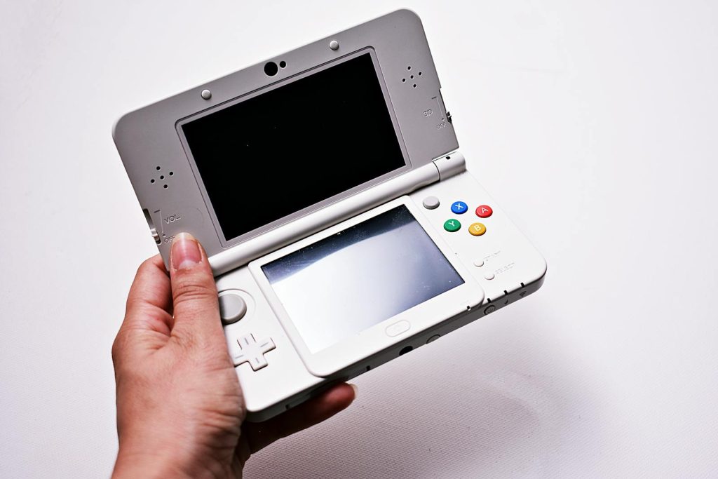 Close-up of a hand holding an open portable gaming console, featuring dual screens.