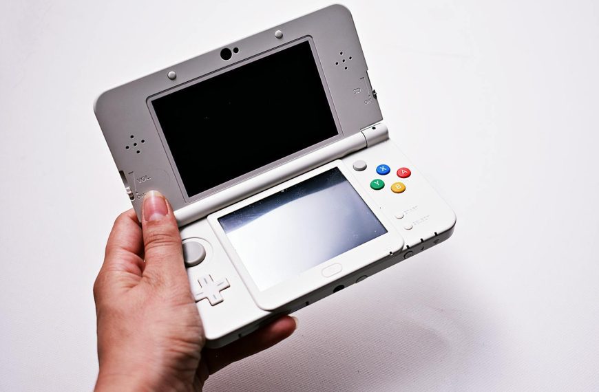 Close-up of a hand holding an open portable gaming console, featuring dual screens.