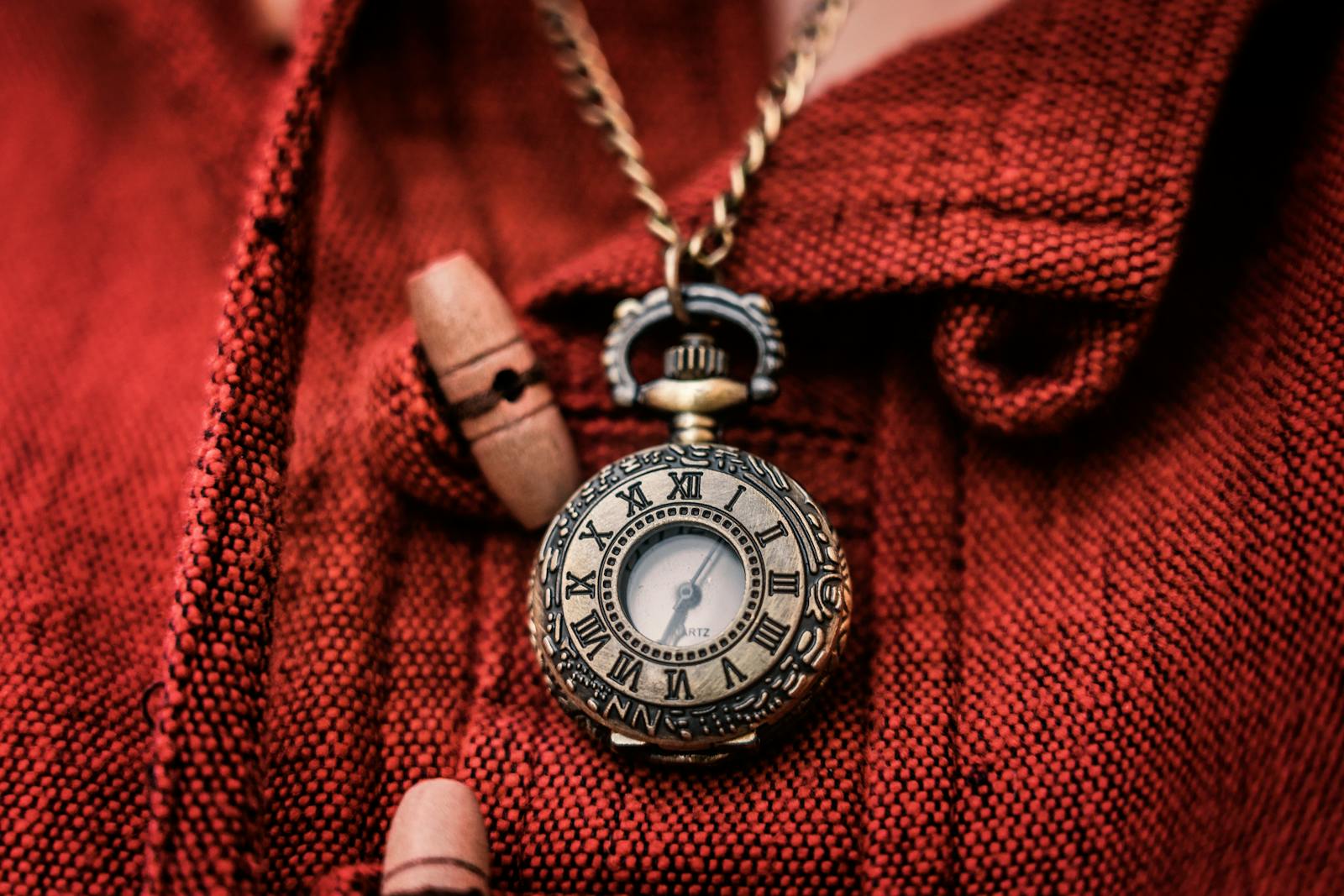 Close-up of a vintage pocket watch with Roman numerals against a textured red background.