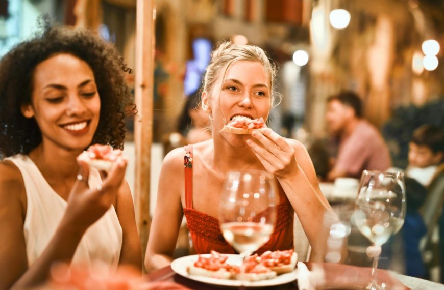 Two women enjoying bruschetta and wine at a vibrant outdoor restaurant.