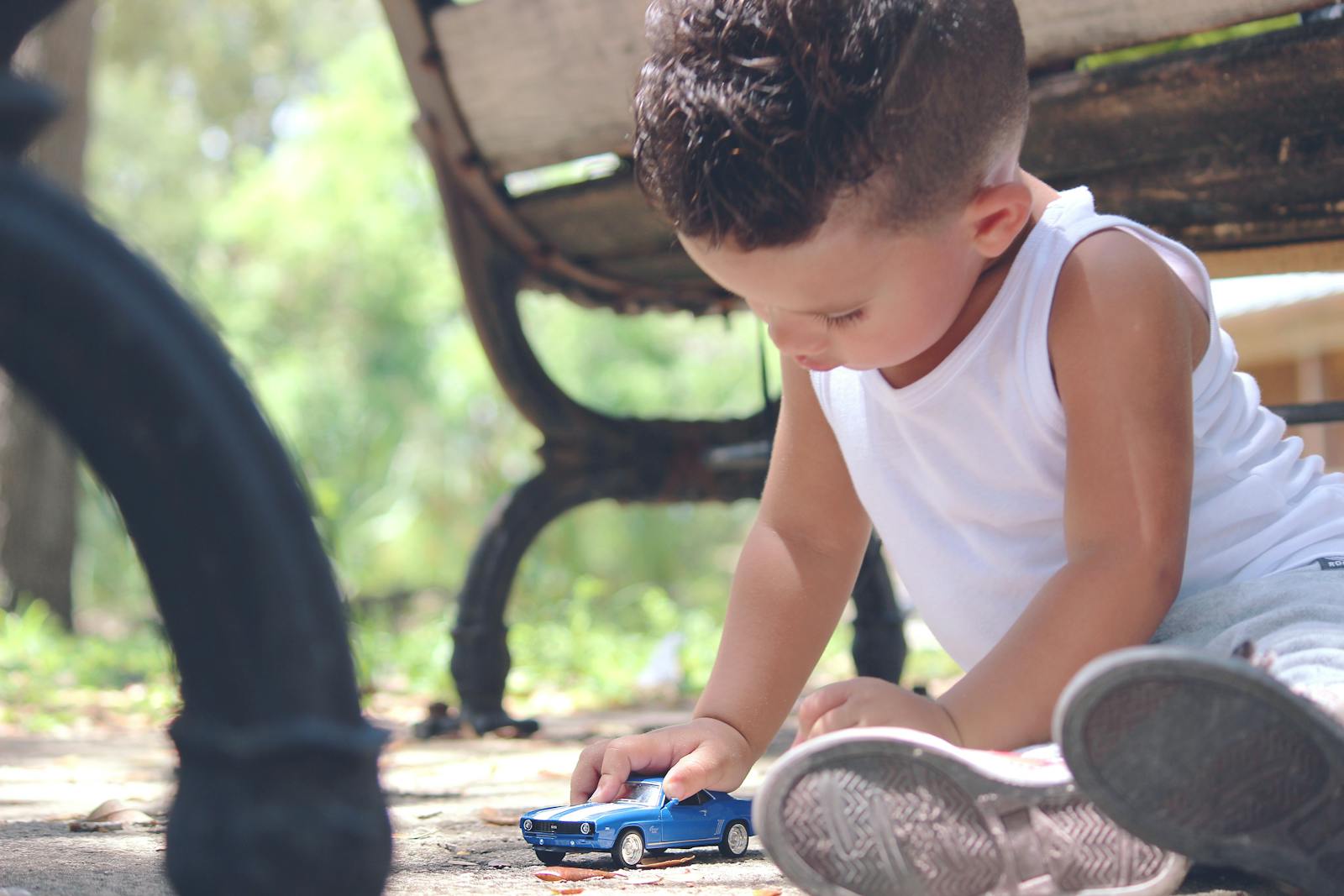 A young boy engaged in imaginative play with a toy car in a sunny park setting.