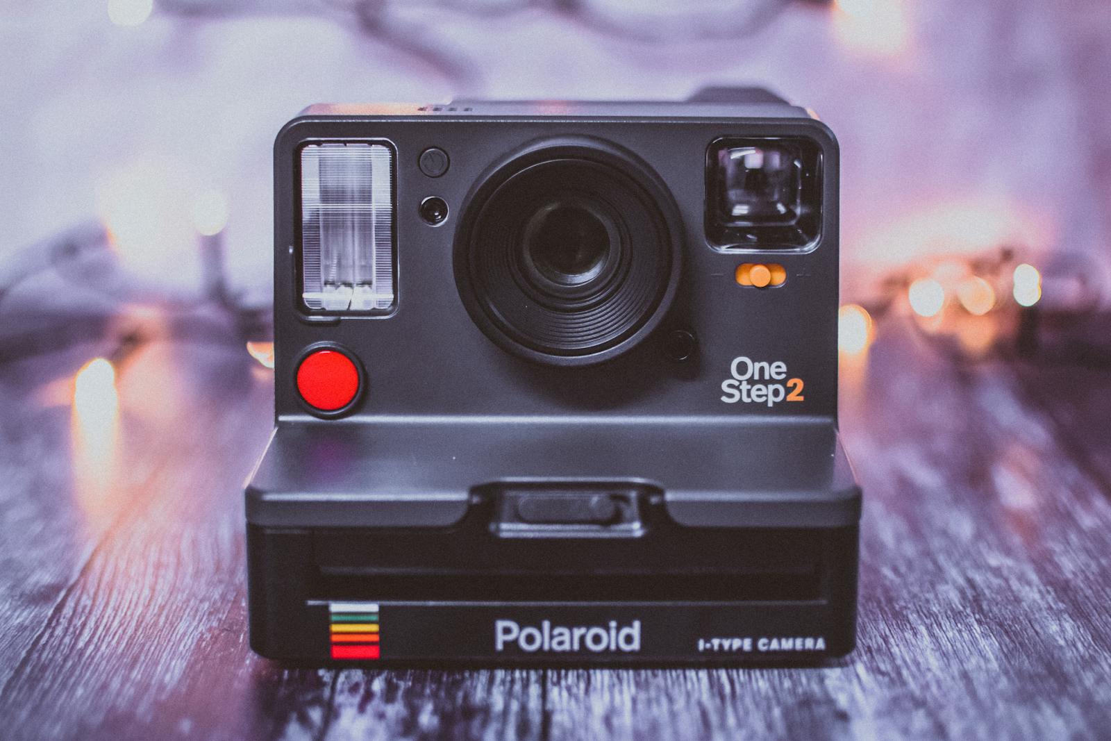 Close-up of a Polaroid OneStep 2 instant camera on a textured wooden surface with bokeh lights.