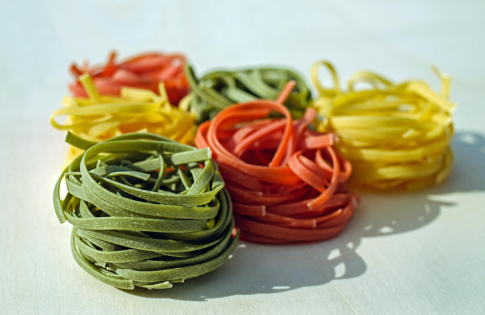 Vibrant multicolored nests of raw pasta on a light surface, showcasing a variety of flavors.