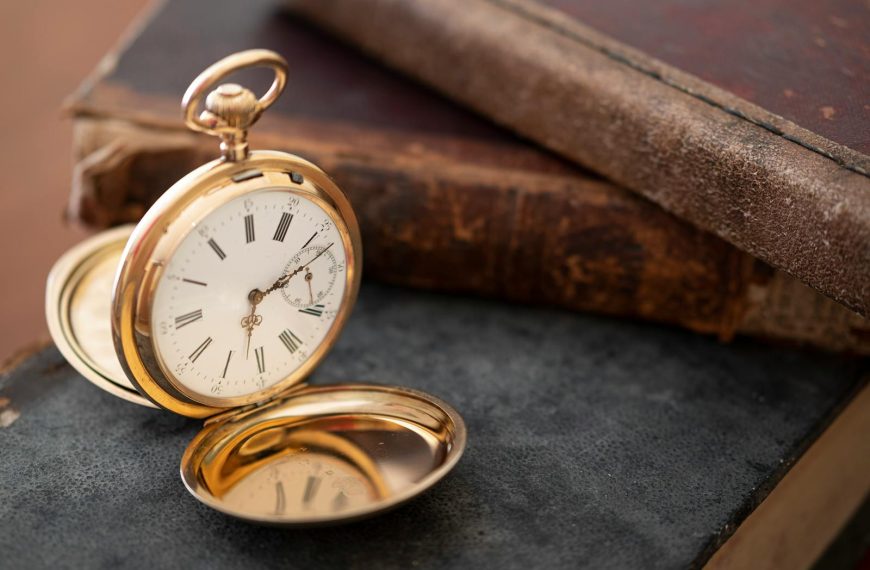 Close-up of a vintage gold pocket watch next to antique books, evoking nostalgia and elegance.