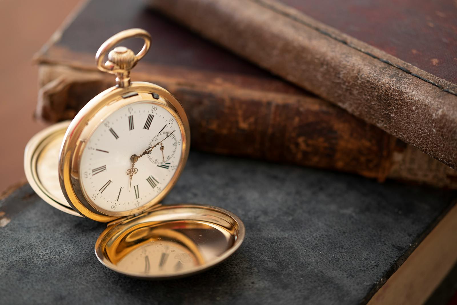 Close-up of a vintage gold pocket watch next to antique books, evoking nostalgia and elegance.