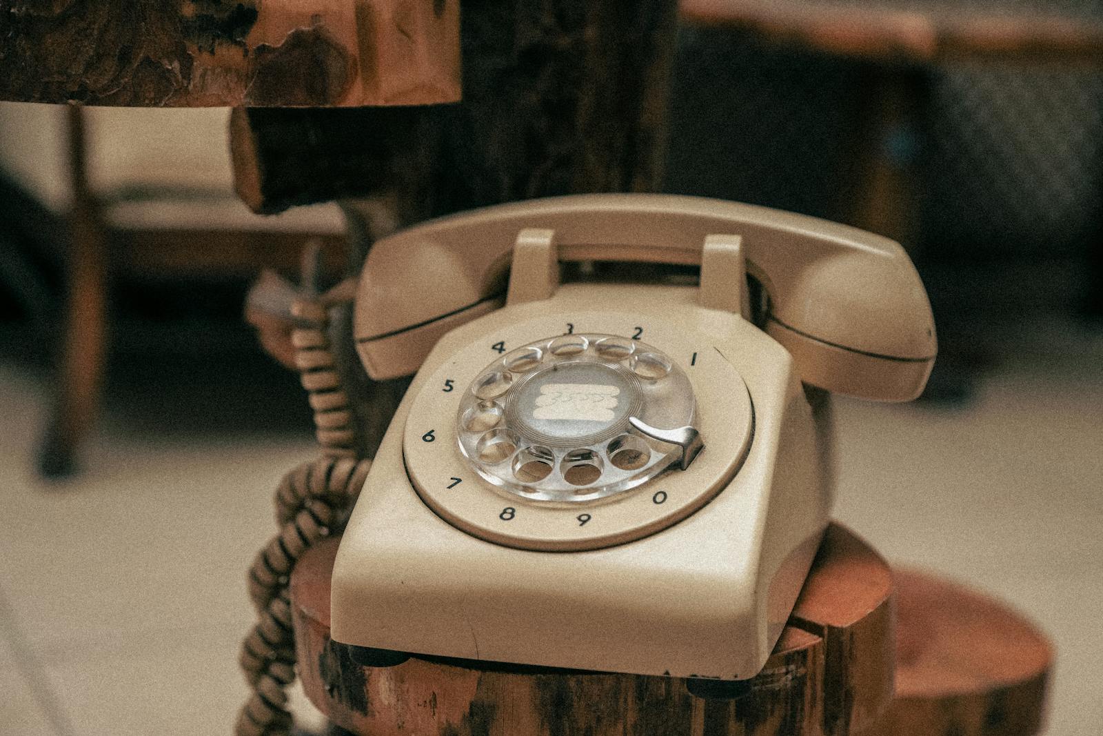 A nostalgic beige rotary dial telephone on a wooden rustic stand evokes a retro vibe.
