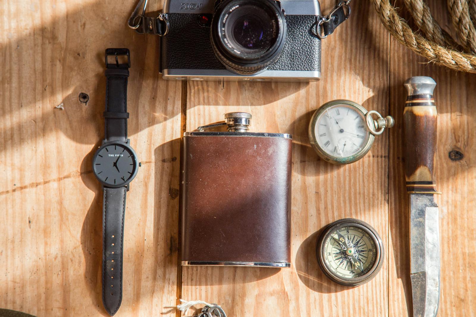 A flat lay of classic items including a camera, pocket watch, and knife on a wooden surface.