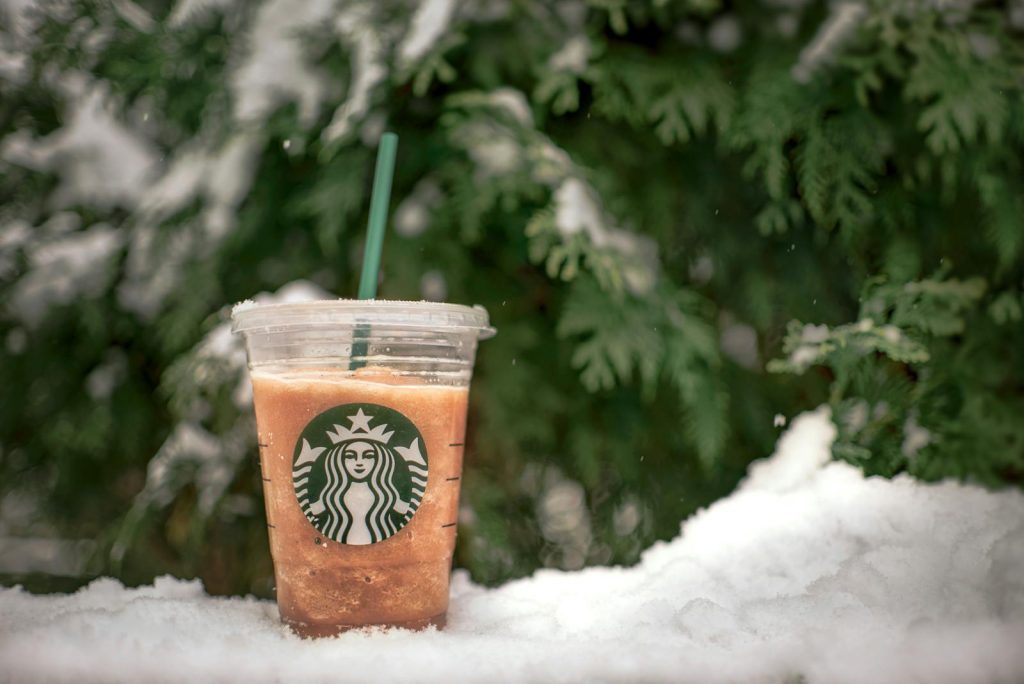 A refreshing iced beverage in a plastic cup set against a snowy evergreen backdrop.