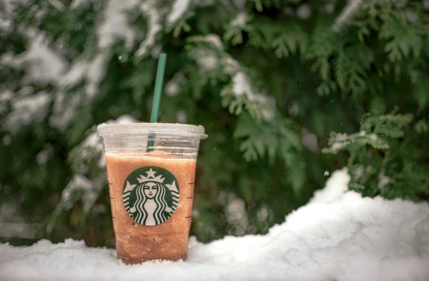 A refreshing iced beverage in a plastic cup set against a snowy evergreen backdrop.