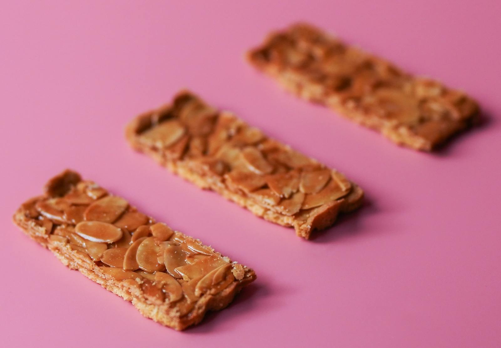 Three delicious almond cookie bars arranged on a vibrant pink surface for a tempting snack display.