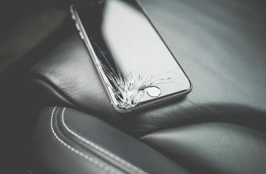Close-up of a broken smartphone with a cracked screen on a leather car seat.