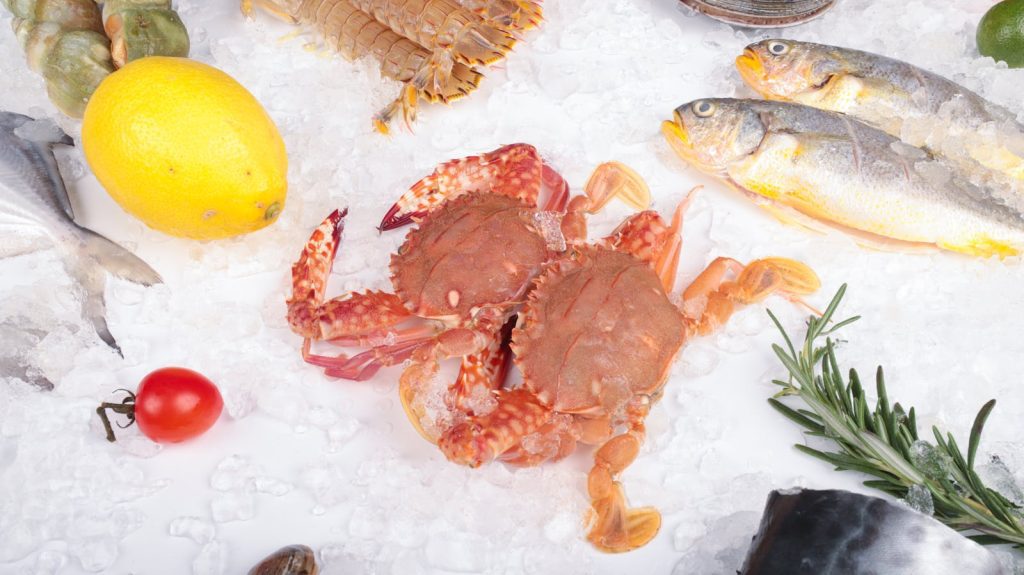 Fresh seafood arrangement with crabs, fish, lemon, and ice on white background.