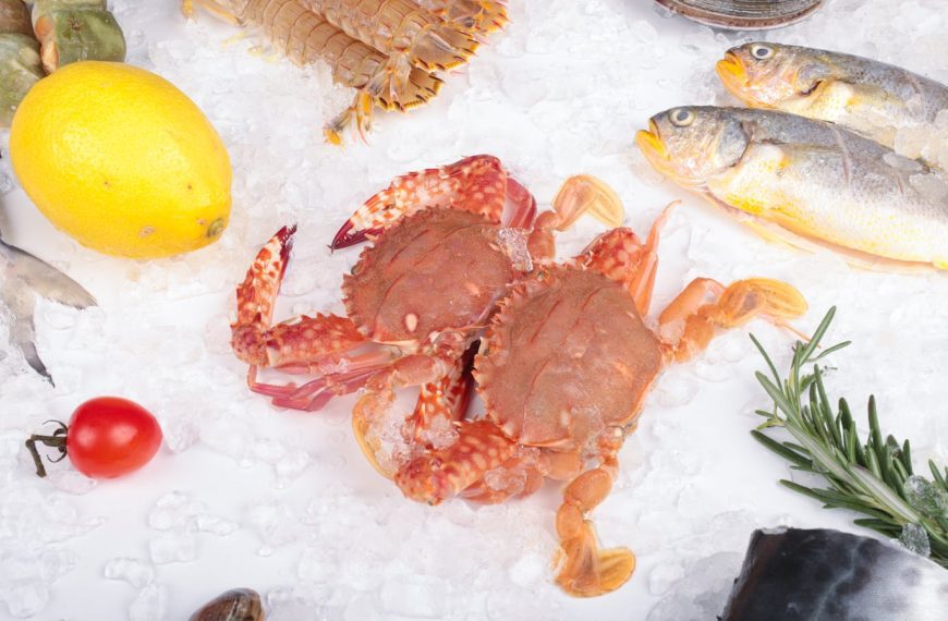 Fresh seafood arrangement with crabs, fish, lemon, and ice on white background.