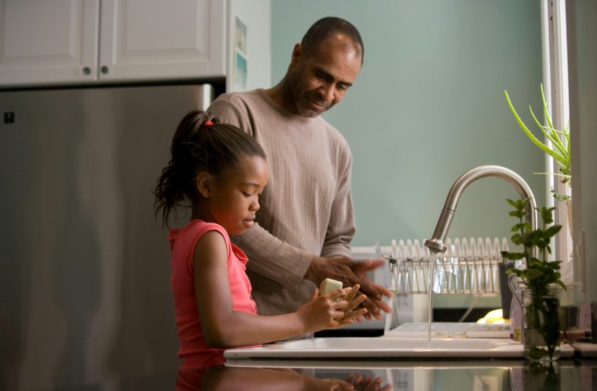 man in long sleeve shirt standing beside girl in pink tank top washing hands