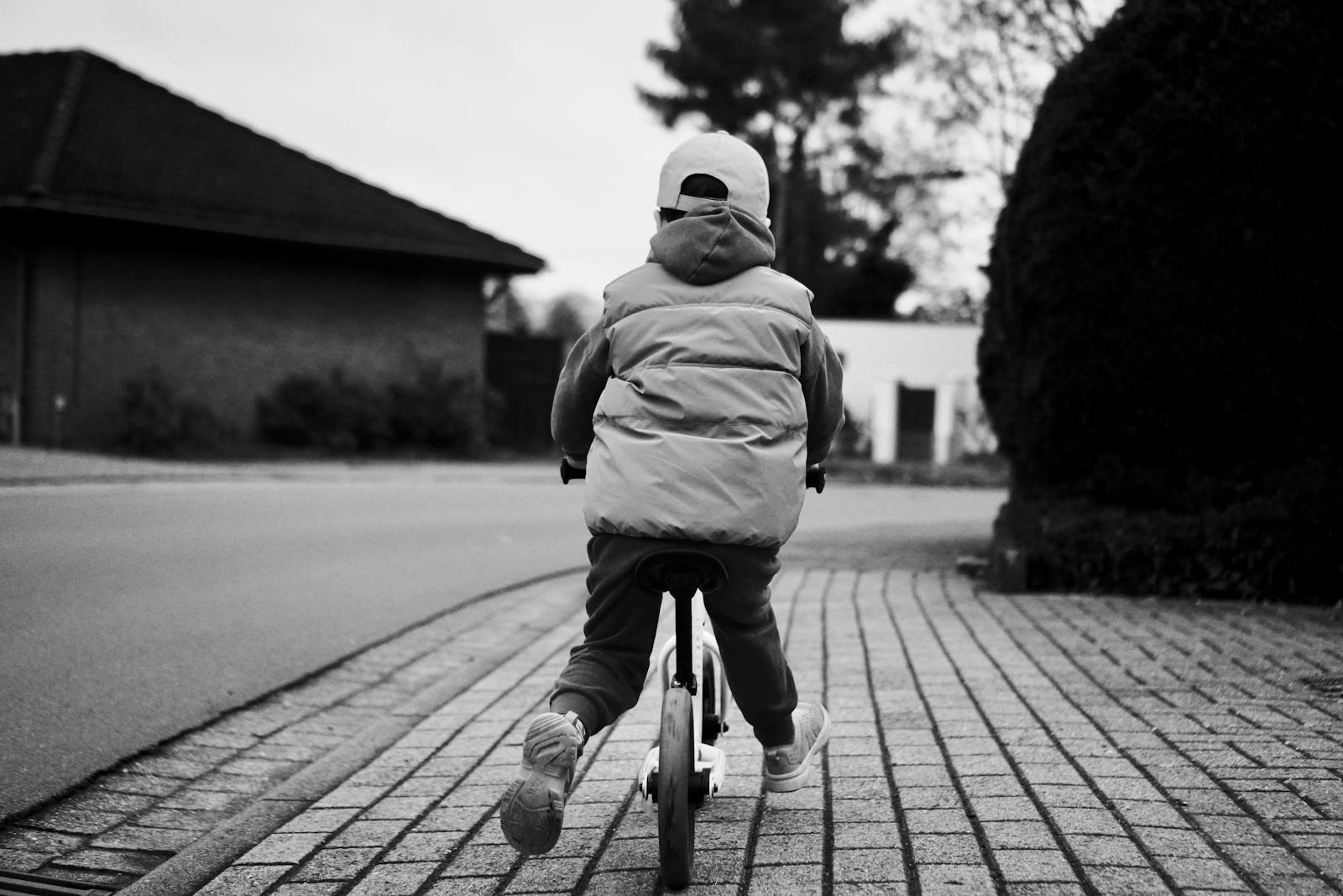 A child riding a bicycle on a city sidewalk captured in black and white, showcasing urban exploration.