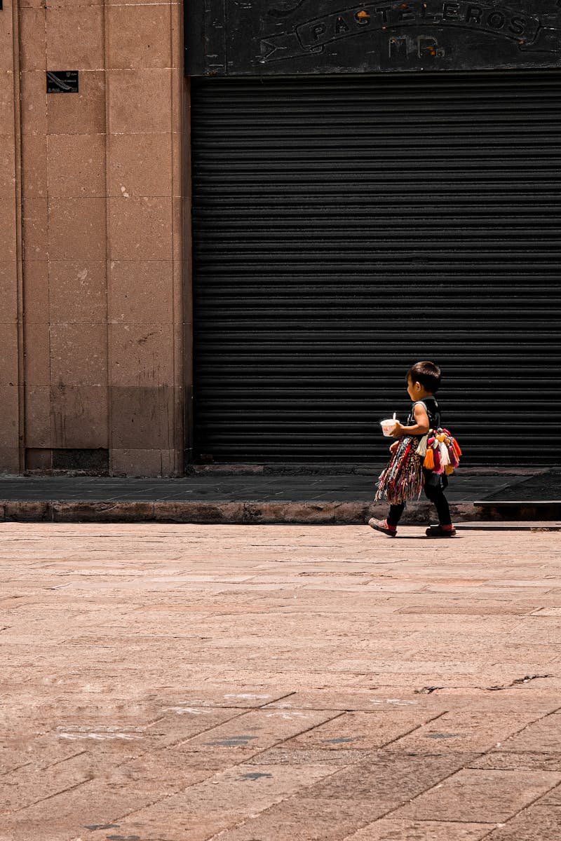 A child carrying a toy walks along an urban street in San Luis Potosí, Mexico, against a closed storefront.