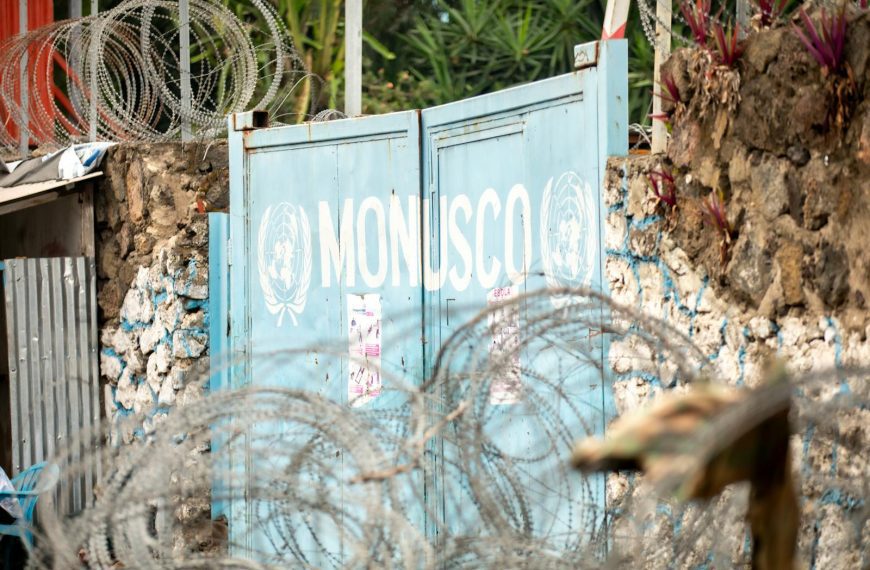 Barbed wire protecting the MONUSCO gate, surrounded by stone walls and plants.