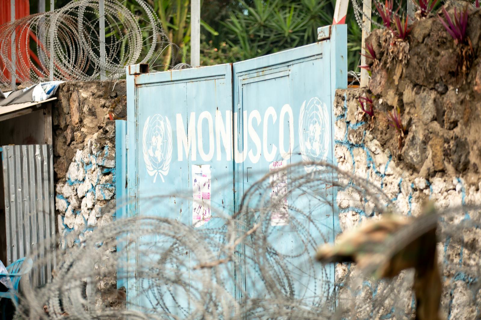 Barbed wire protecting the MONUSCO gate, surrounded by stone walls and plants.