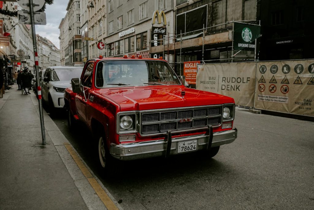 Classic red GMC truck parked on a bustling European street with urban backdrop.