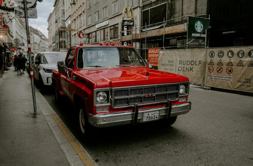 Classic red GMC truck parked on a bustling European street with urban backdrop.