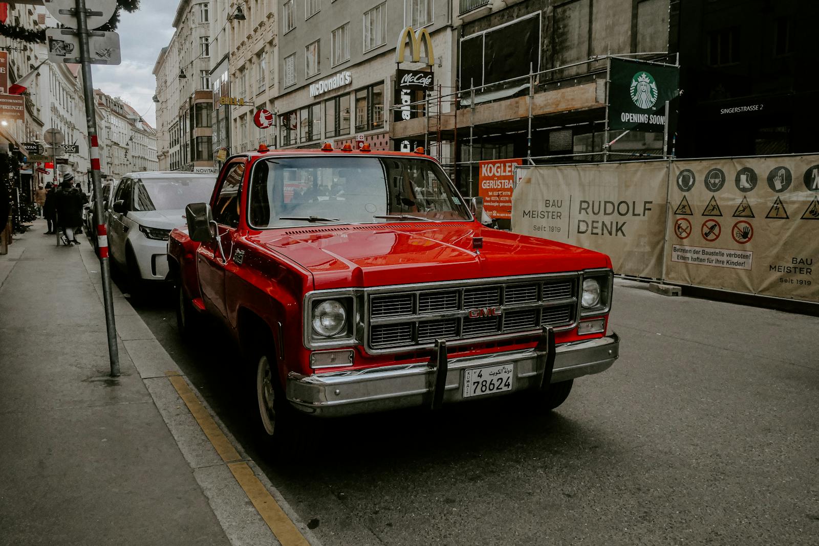 Classic red GMC truck parked on a bustling European street with urban backdrop.