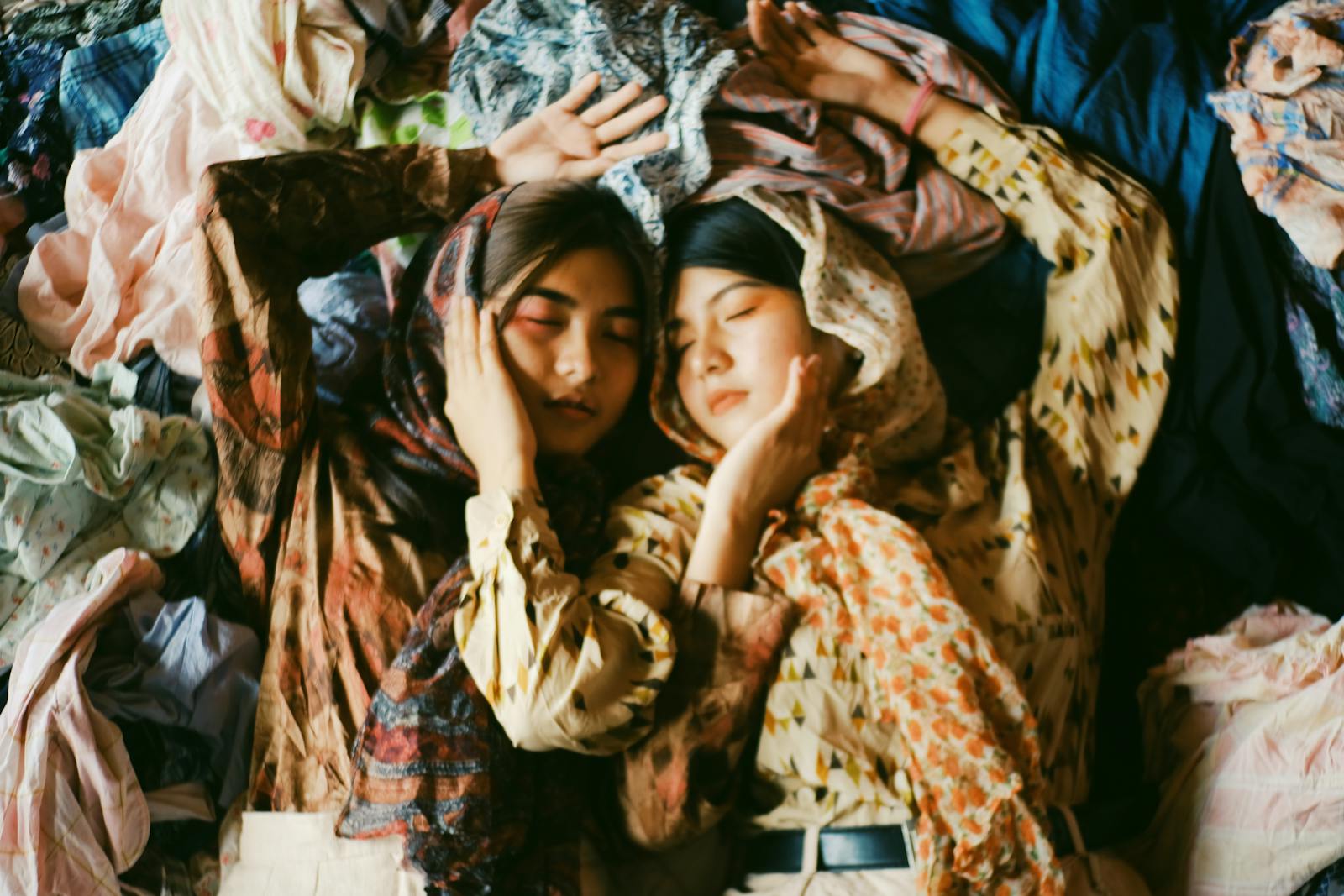 Two women peacefully resting amidst vibrant fabrics, showcasing multicultural harmony and artistic expression.